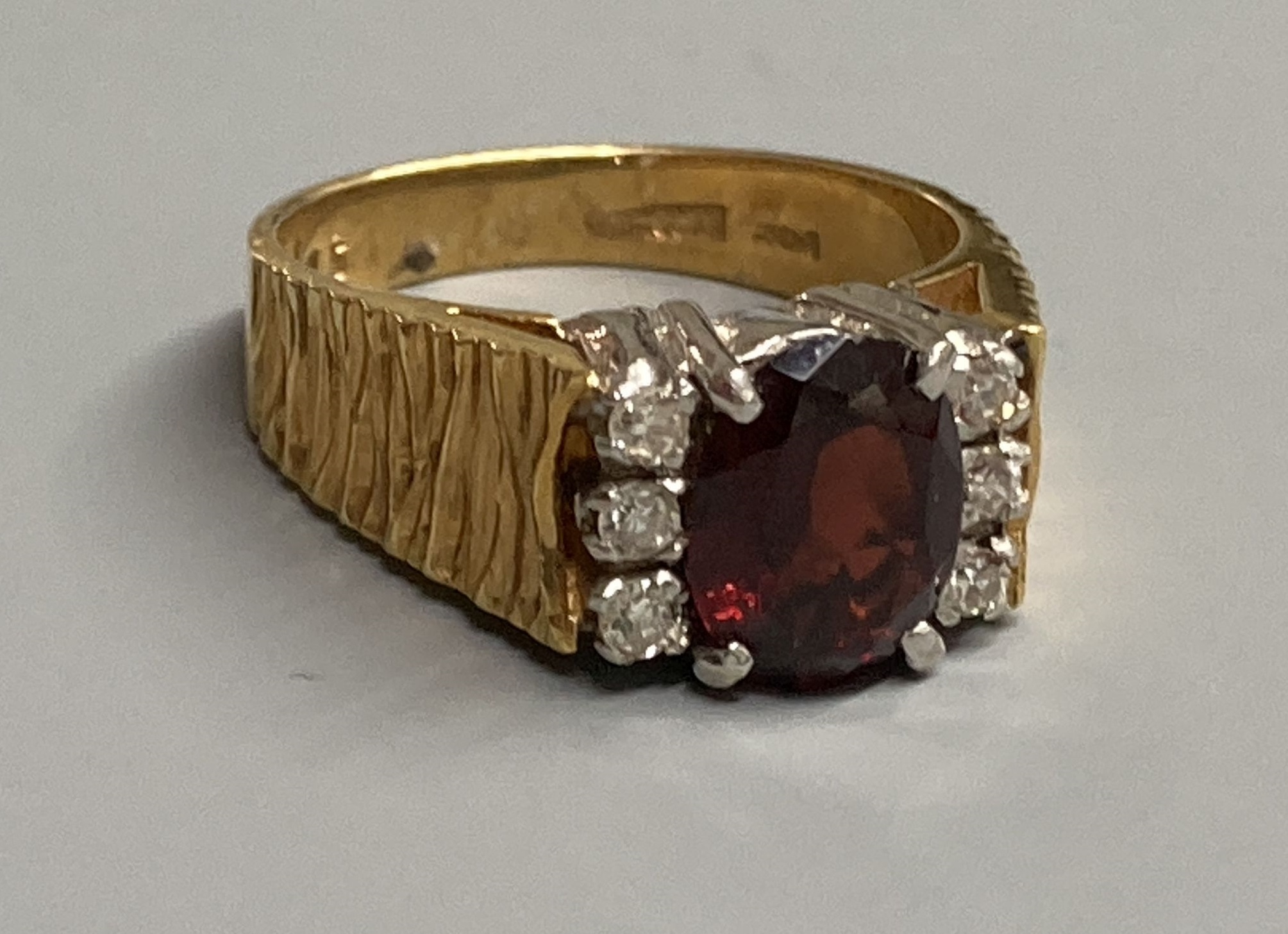 A 1970's 18ct gold, garnet and diamond cluster ring, with textured shoulders, size N/O, gross 7.9 grams.